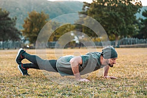 Sports and yoga. A man in sportswear push-ups during training. Park and trees on the background. View at profile