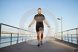sportsman in activewear jumps with skipping rope at sea pier