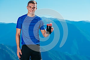 Sportsman athlete drinking water on top of a mountain while enjoying the amazing view of the lake