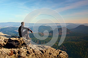 Sportsman in black sit on the peak of sandstone rock in rock empires park and watching over the misty and foggy morning valley photo