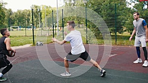 Sportsman in black uniform playing basketball outdoors with friends, dribbling and scoring goal