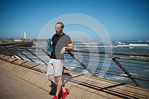 Sportsman with a bottle of water on the beach after morning jog or bodyweight training on the outdoor sportsground