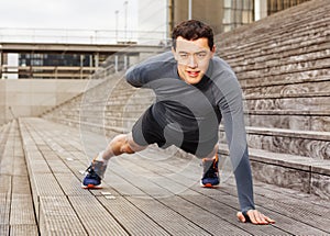 Sportsman doing push-ups on one hand outdoors