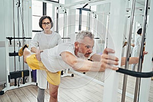 Sportsman doing a strength training exercise assisted by a physiatrist