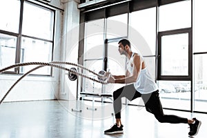 Sportsman exercising with battle ropes in modern gym