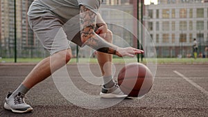 Sportsman in grey shorts bounces ball on basketball court against football field