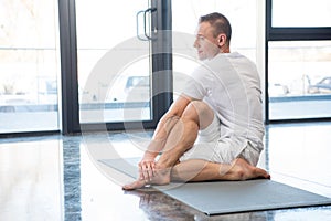 Sportsman in half spinal twist pose sitting on yoga mat