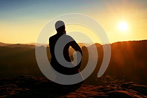 Sportsman hiker in black sportswear sit on mountain top and take a rest. Tourist watch down to morning misty valley.