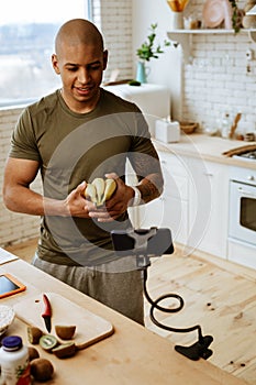 Sportsman holding bunch of bananas filming video about healthy diet