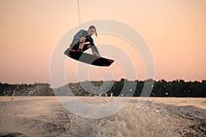 sportsman making trick in jump time with wakeboard on sky background.