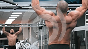 Sportsman performing pull-ups on bars during cross-training workout at gym. bodybuilder looks mirror and pulls up on crossbar fitn