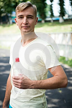 Sportsman with plastic bottle on sunny outdoor. Thirsty man with water bottle on stadium. Thirst and dehydration. Drinking water f