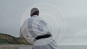 Sportsman practicing hands punches on gloomy beach. Focused man workout karate.