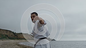 Sportsman practicing hands punches on gloomy beach. Focused man workout karate.
