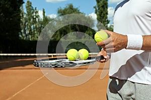 Sportsman with racket and tennis balls at court, closeup