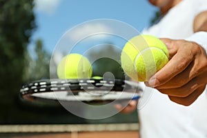 Sportsman with racket and tennis balls at court, closeup