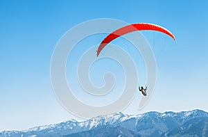 Sportsman on red paraglider soaring over the snowy mountain peak