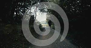 Sportsman running on dark autumn forest road. Young athlete on quiet autumn deserted pass. Cinematic drone back view.