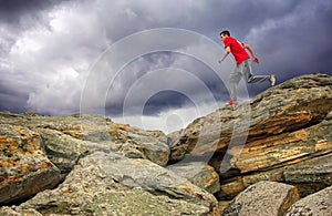 Sportsman running, jumping over rocks in mountain area.