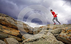 Sportsman running, jumping over rocks in mountain area.