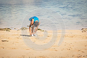 sportsman with smartphone armband tying shoelaces on beach