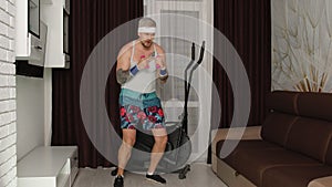 Sportsman stylish fat guy in funny clothes making boxing exercises with dumbbells in place at home