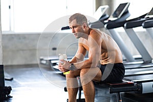 Sportsman  taking a break after running on treadmill machine at the gym sitting  and drinking gatorade water at sport club.