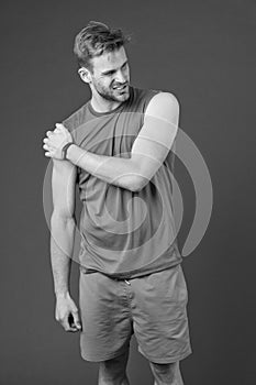 Sportsman touch shoulder on violet background. Muscular man feel pain after training or workout. Pain in shoulder. Sport