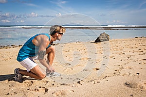 sportsman tying shoelaces on sneakers on beach