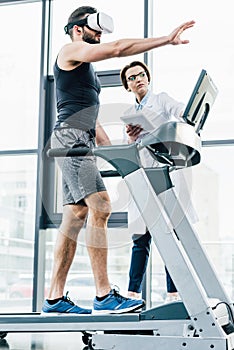 sportsman in vr headset gesturing on treadmill near doctor during endurance test in gym.