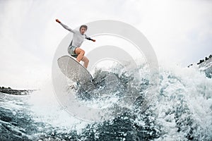 sportsman in wetsuit go in for active water sport and wave on wakesurf board