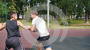 Sportsman in white t-shirt playing basketball on the court outdoors with friend, dribbling and throwing the ball