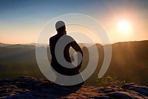 Sportsmann hiker in black sportswear sit on mountain top and take a rest. Tourist watch down to morning misty valley.