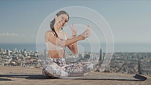 Sportsoman taking selfie on smartphone at city. Yoga woman sitting in lotus pose