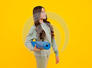 Sportswear advertising concept. Teenager child girl in tracksuits jogging suit posing in the studio hold fitness mat.