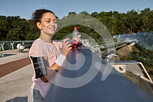 Sportswoman, athlete with a bottle of water in her hand after intense cardio workout and morning jog, looking away resting on a