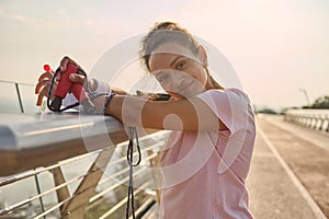 Sportswoman with a bottle of water and jumping rope after intense cardio workout and morning jog, looking away resting on a city