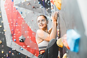 Sportswoman climber moving up on steep rock, climbing on artificial wall indoors. Extreme sports and bouldering concept