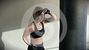The sportswoman confidently strikes her hands in the boxing bag in the gym