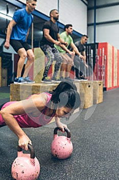 Sportswoman doing push-ups with kettlebells