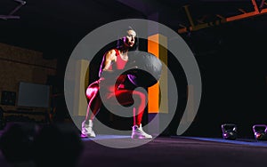 Sportswoman doing squat exercises with fitness ball. Female exercising and stretching with medicine ball at gym