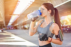 Sportswoman drinking water after sports training outdoors.