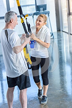 Sportswoman holding sport bottle and senior sportsman with resistance band talking