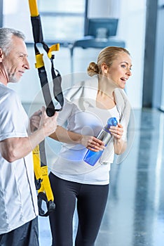 Sportswoman holding sport bottle and senior sportsman with resistance band talking