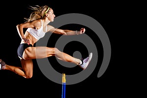 Sportswoman jumping over hurdle on sprint race