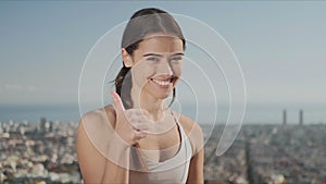 Sportswoman showing thumbs up sign. Fitness woman looking at camera outside