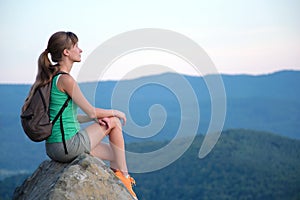 Sportswoman sitting alone taking a break on hillside trail. Female hiker enjoying view of evening nature from rocky