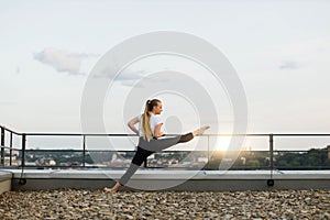 Sportswoman spreading legs in front splits on roof handrail