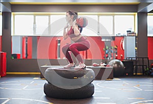 Sportswoman squatting with bag on tyres