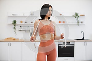 Sportswoman stretching measuring tape on shoulders at home